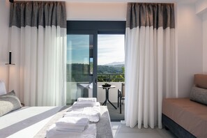 A hotel room with a bed, a sofa, a small table with a plant, and a balcony with a view of the landscape. - Queen Bee Villa - Four Bedroom Villa, Sleeps 10 (Prinos)