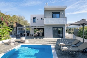 A modern two-story house with a swimming pool, outdoor seating, and a view of the landscape. - Queen Bee Villa - Four Bedroom Villa, Sleeps 10 (Prinos)