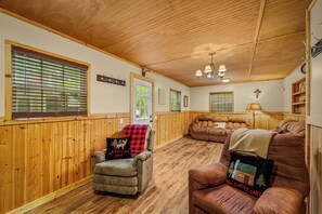 A cozy room with wooden walls and ceiling, a fireplace, a sofa, a chair, and a lamp. - Cash Cabins-sleeps 13 in 2 cabins (Mentone)