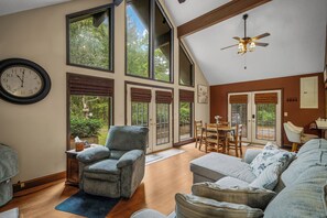 A spacious living room with a large window, a ceiling fan, and a dining area with a table and chairs. - Cash Cabins-sleeps 13 in 2 cabins (Mentone)