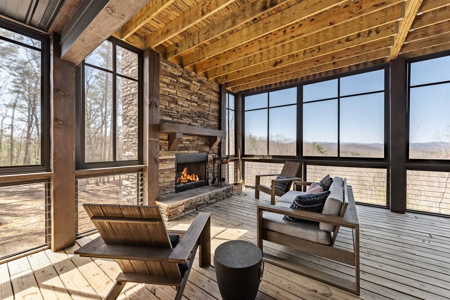 A wooden deck with a stone fireplace, seating, and large windows.