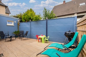 A patio area with a blue wall, a table with chairs, a barbecue grill, and a wooden fence. - Villa Mont Plaisir, just a stone's throw from the beach. Pets allowed. (Langrune-sur-Mer)