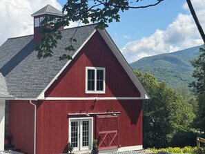 A red barn with a white door and window, a chimney, and a view of a mountain range. - The Carriage Barn: new build with expansive mountain views and walk to Dorset (Dorset)