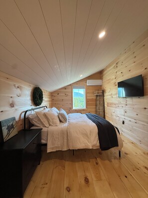 A bedroom with a bed, bedside table, and a TV mounted on the wall. - The Carriage Barn: new build with expansive mountain views and walk to Dorset (Dorset)