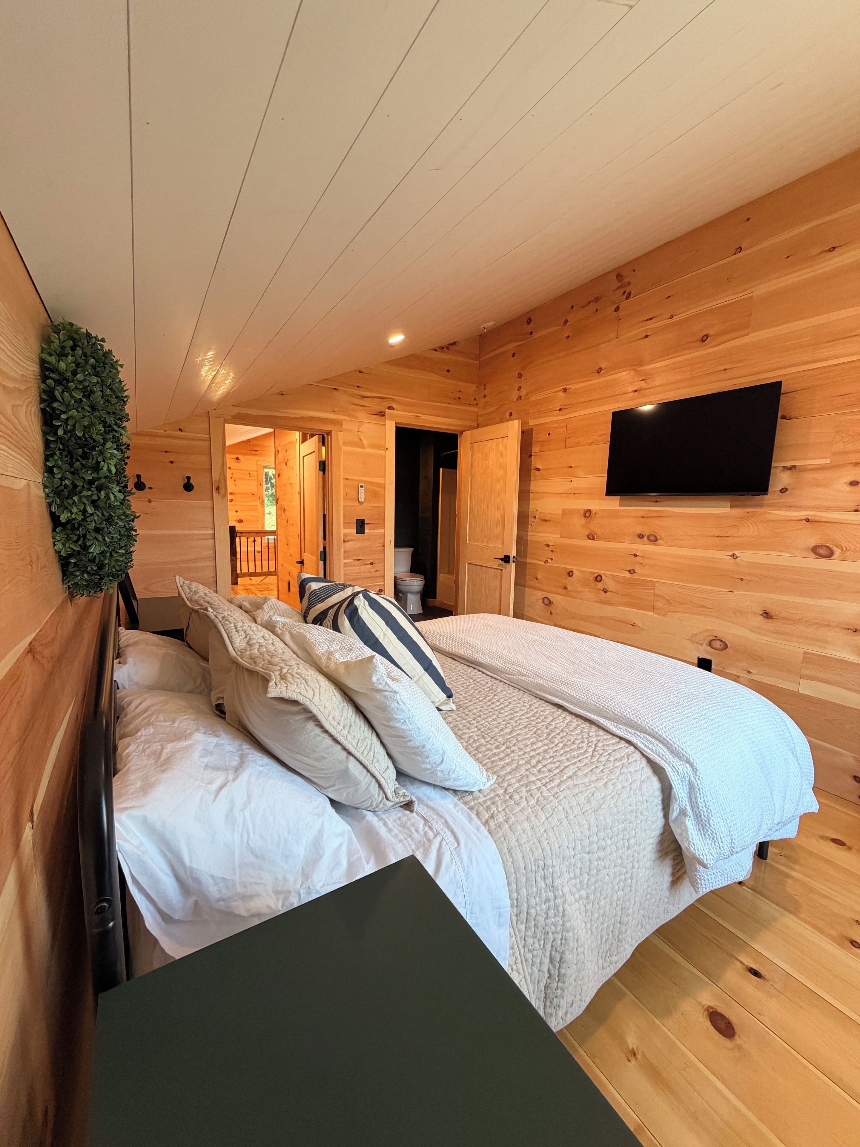 A wooden cabin bedroom with a bed, pillows, a TV, and a small table.