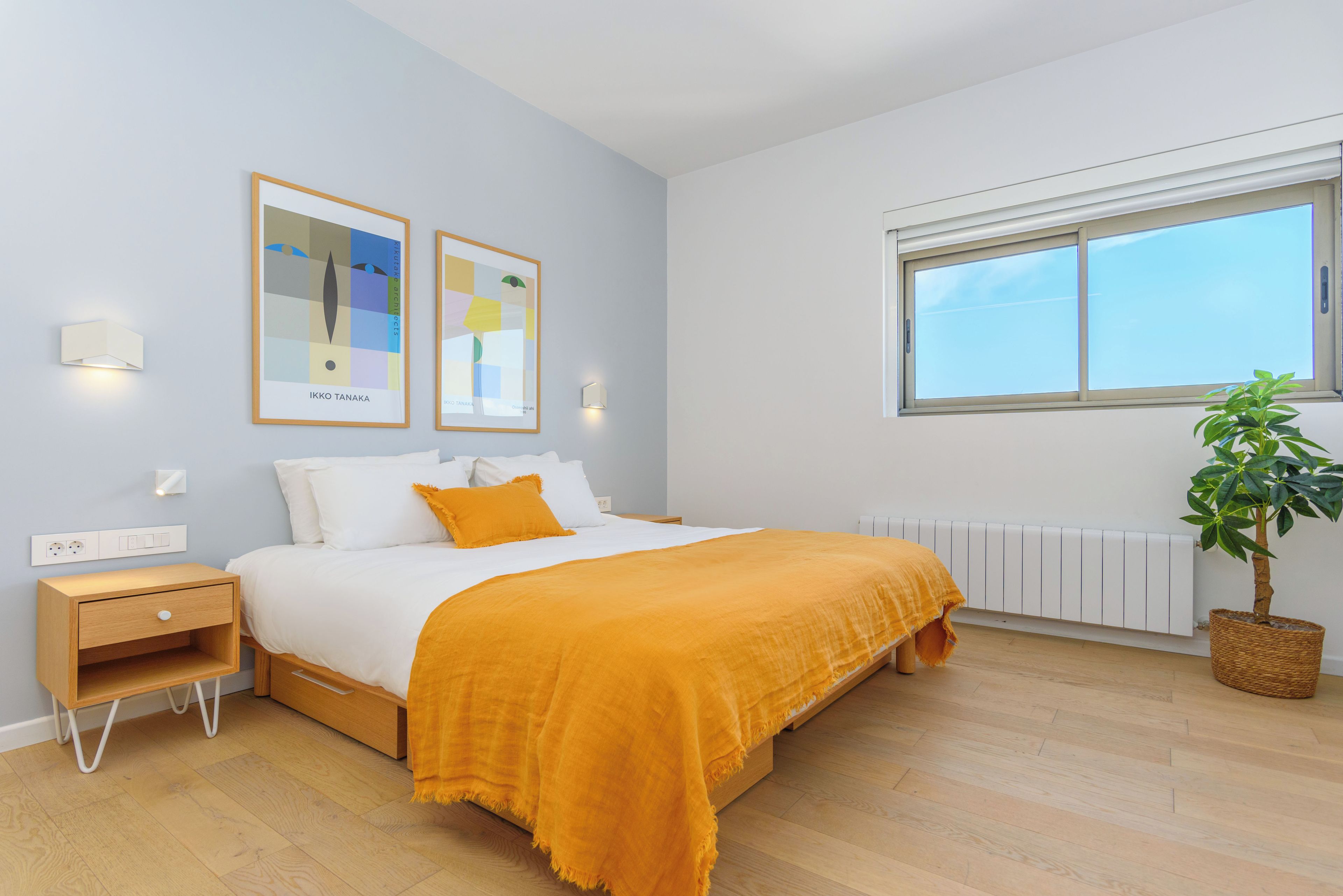Een slaapkamer met een bed, nachtkastjes, een radiator, een raam en een kamerplant.