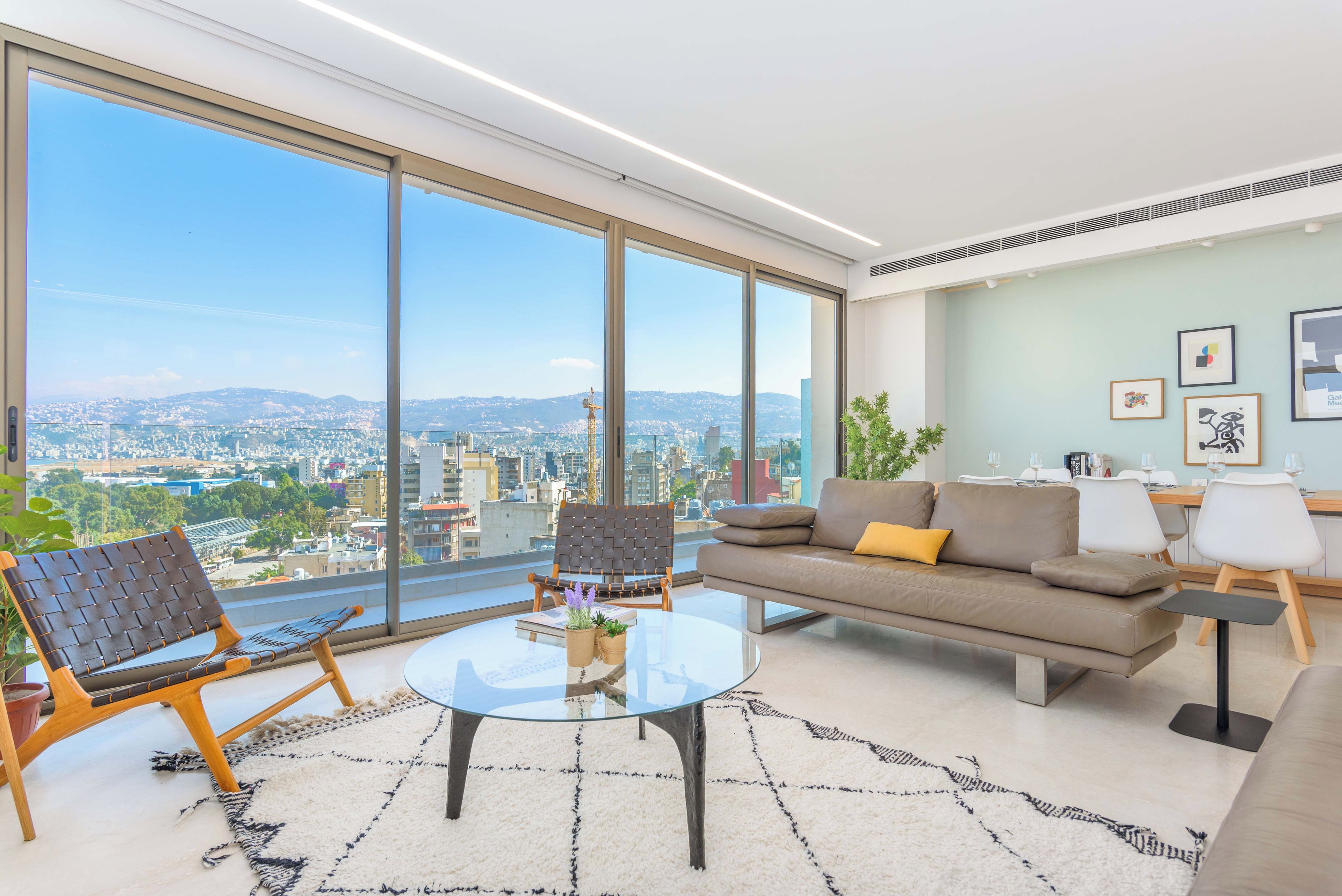 Un salon moderne avec une table basse en verre, un canapé et une vue sur le paysage urbain, visible à travers de grandes fenêtres.