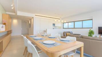 A modern dining area with a wooden table set for four, white chairs, and a kitchen in the background.