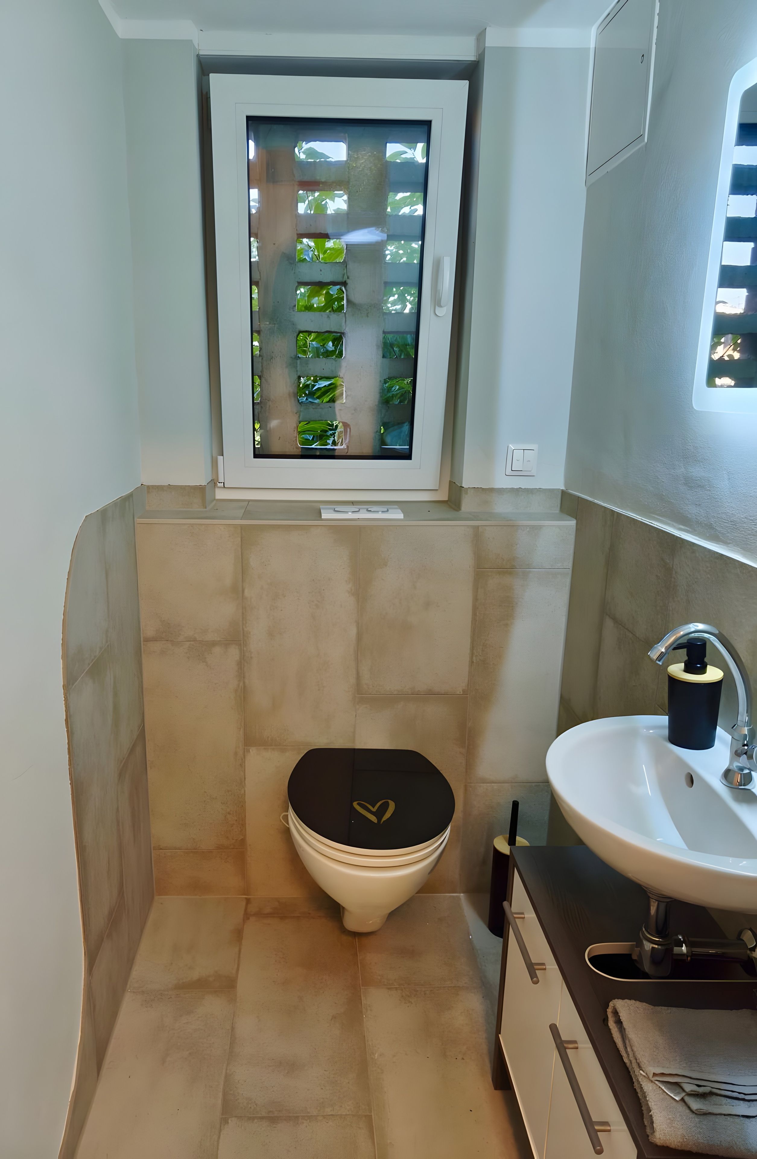 Ein kleines Badezimmer mit Toilette, Waschbecken und einem Fenster mit Blick auf Grünflächen.