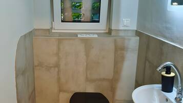Ein kleines Badezimmer mit Toilette, Waschbecken und einem Fenster mit Blick auf Grünflächen.