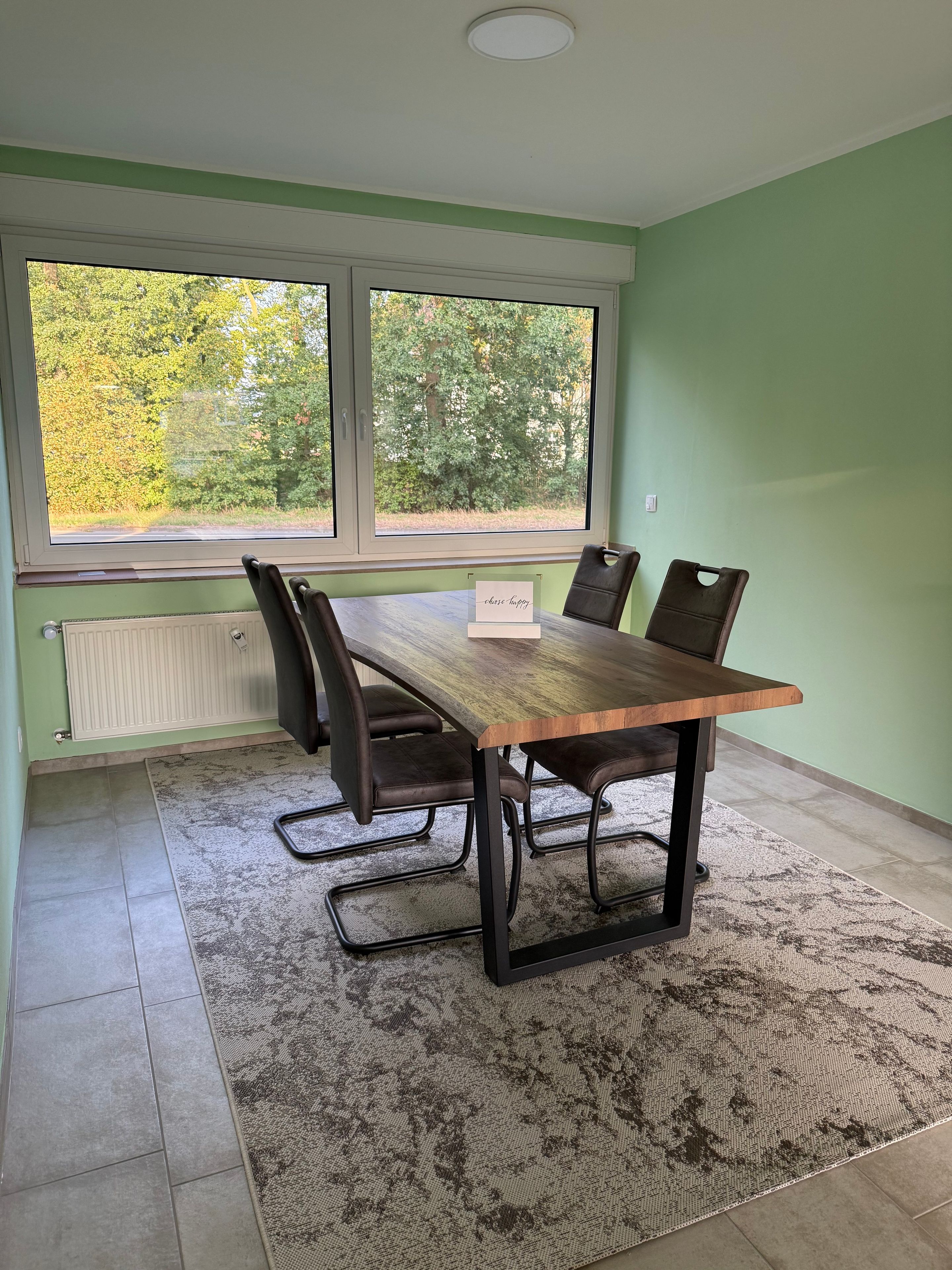 Ein Konferenzraum mit einem langen Tisch, vier Stühlen und Blick auf Bäume durch große Fenster.