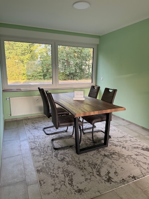 Ein Konferenzraum mit einem langen Tisch, vier Stühlen und Blick auf Bäume durch große Fenster.