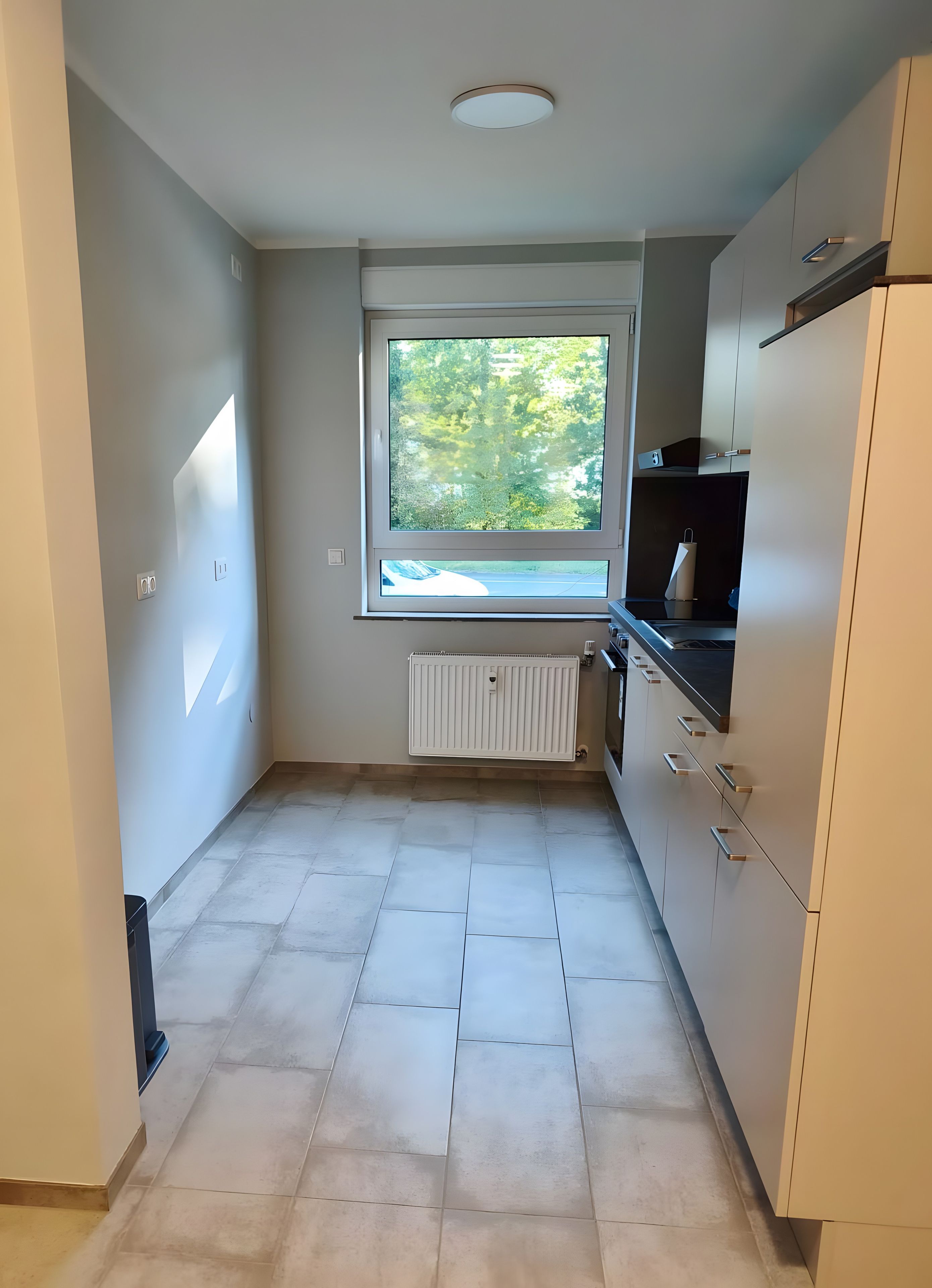 Eine Küche mit Fenster, weißen Schränken und einer Heizung.