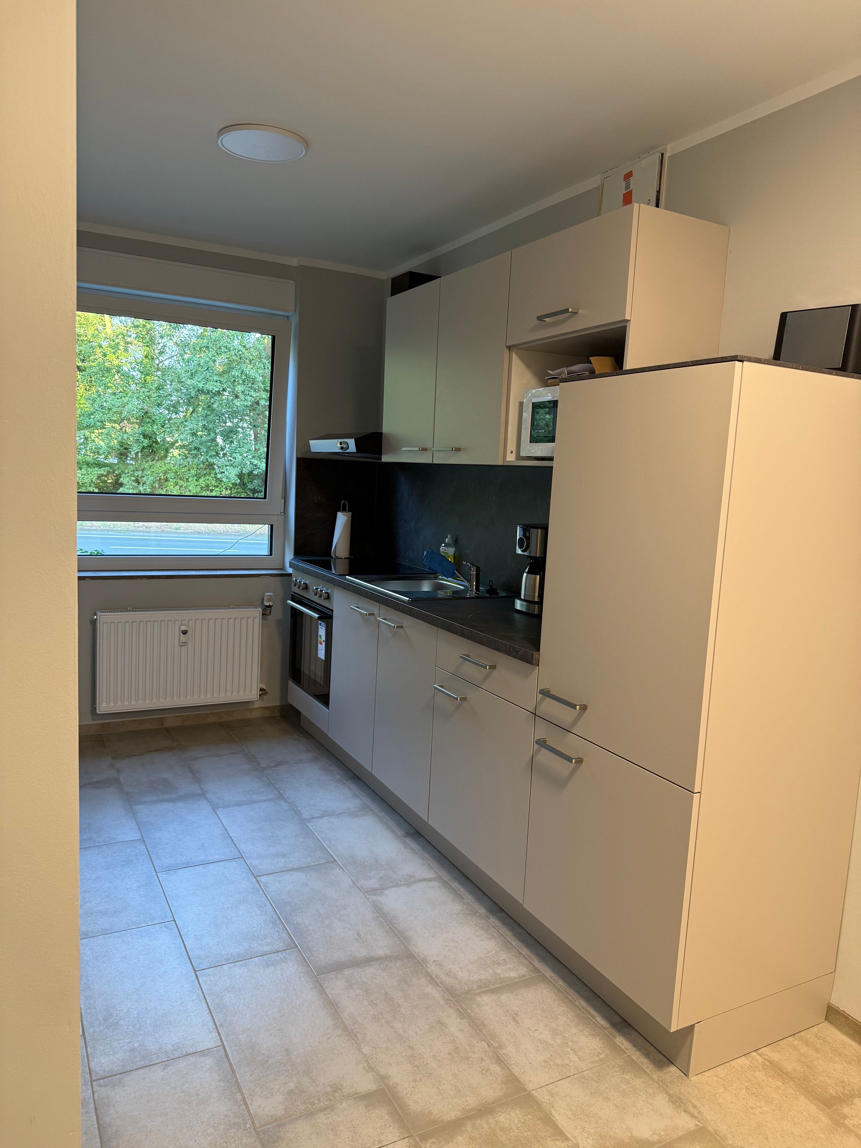 A modern kitchen with a window, built-in appliances, and a tiled floor.