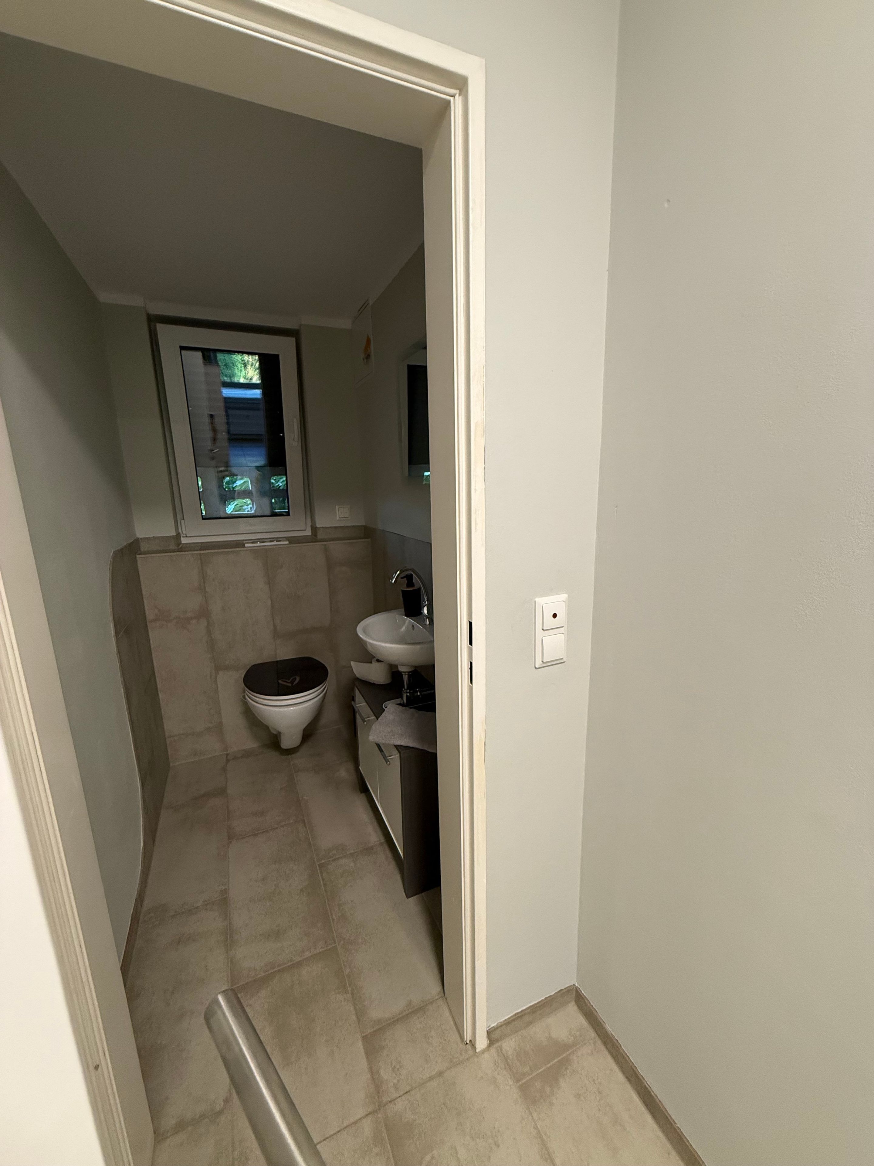 Ein schmales Badezimmer mit Toilette, Waschbecken und Fenster.
