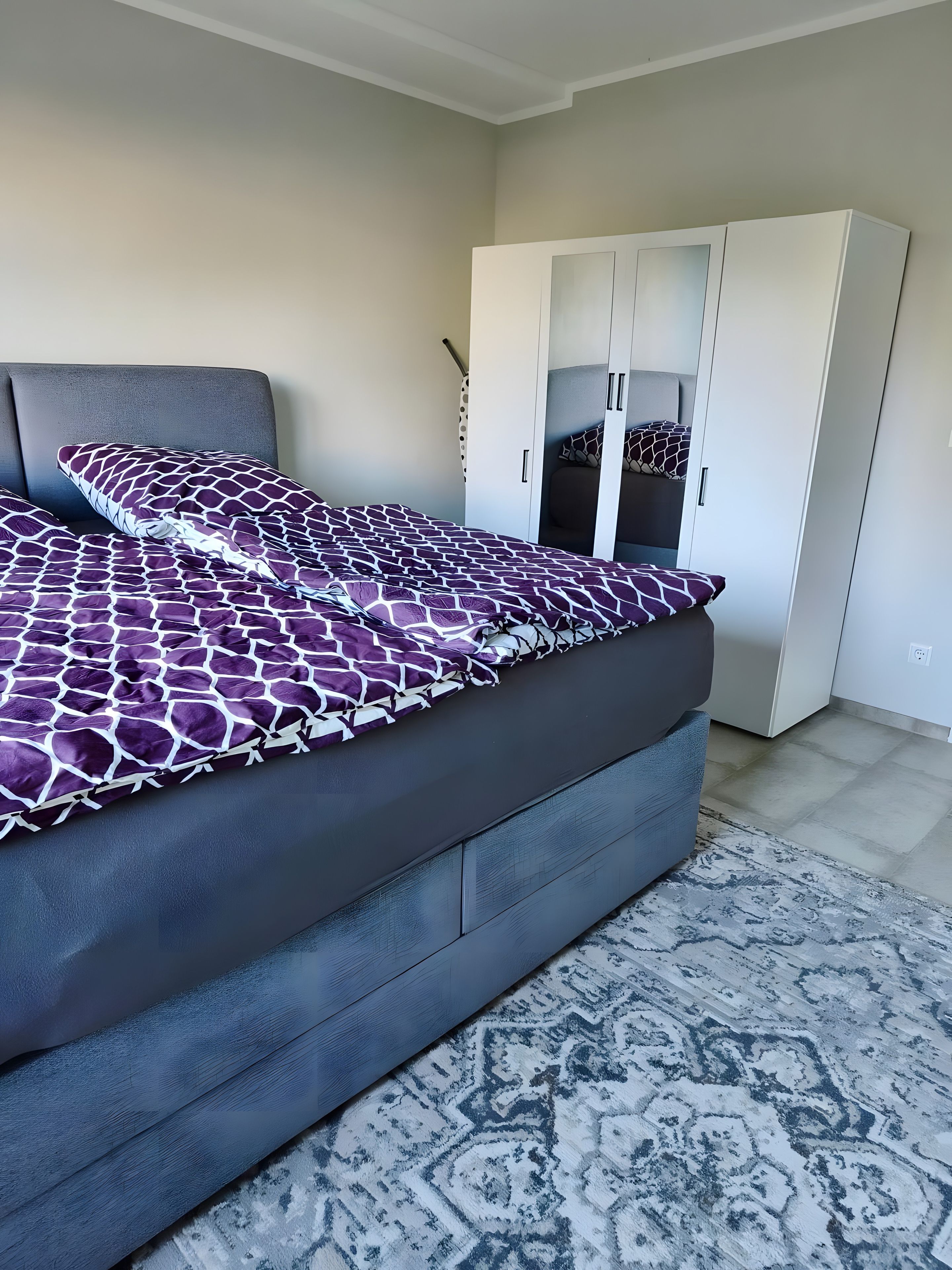 A bedroom with a bed, a wardrobe, and a patterned rug.