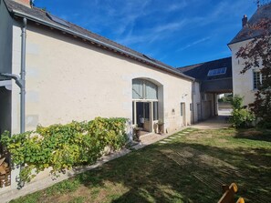 Ein Gebäude mit einem gepflasterten Weg, einem überdachten Eingang und einem Gartenbereich mit Hecke und Blumentöpfen.