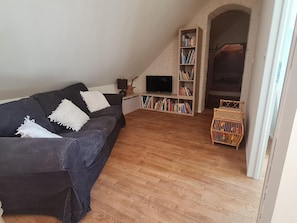 Een woonkamer met een donkere bank, een boekenkast, een televisietoestel en een houten vloer.