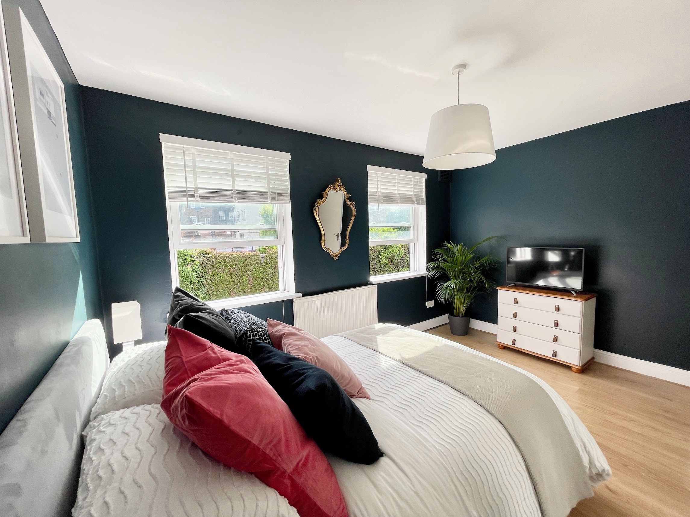 A modern bedroom with a bed, a dresser, a television, and a large window.