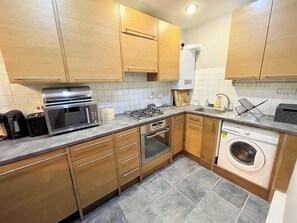 A compact kitchen with wooden cabinets, a built-in microwave, a gas stove, a dishwasher, and a washing machine. - Bright Home Near Central London - Near Emirates Stadium (London)