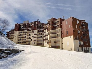 Um edifício residencial de vários andares com varandas, localizado numa encosta coberta de neve.