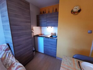 Eine kompakte Küche mit Einbauherd, einer kleinen Spüle und einer Mikrowelle. Es gibt einen Holzkasten und eine an der Wand befestigte Uhr.
