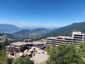Ein Hotel mit mehreren Etagen, einer Außenbereich-Sitzgelegenheit mit Sonnenschirmen und Blick auf die umliegenden Berge.