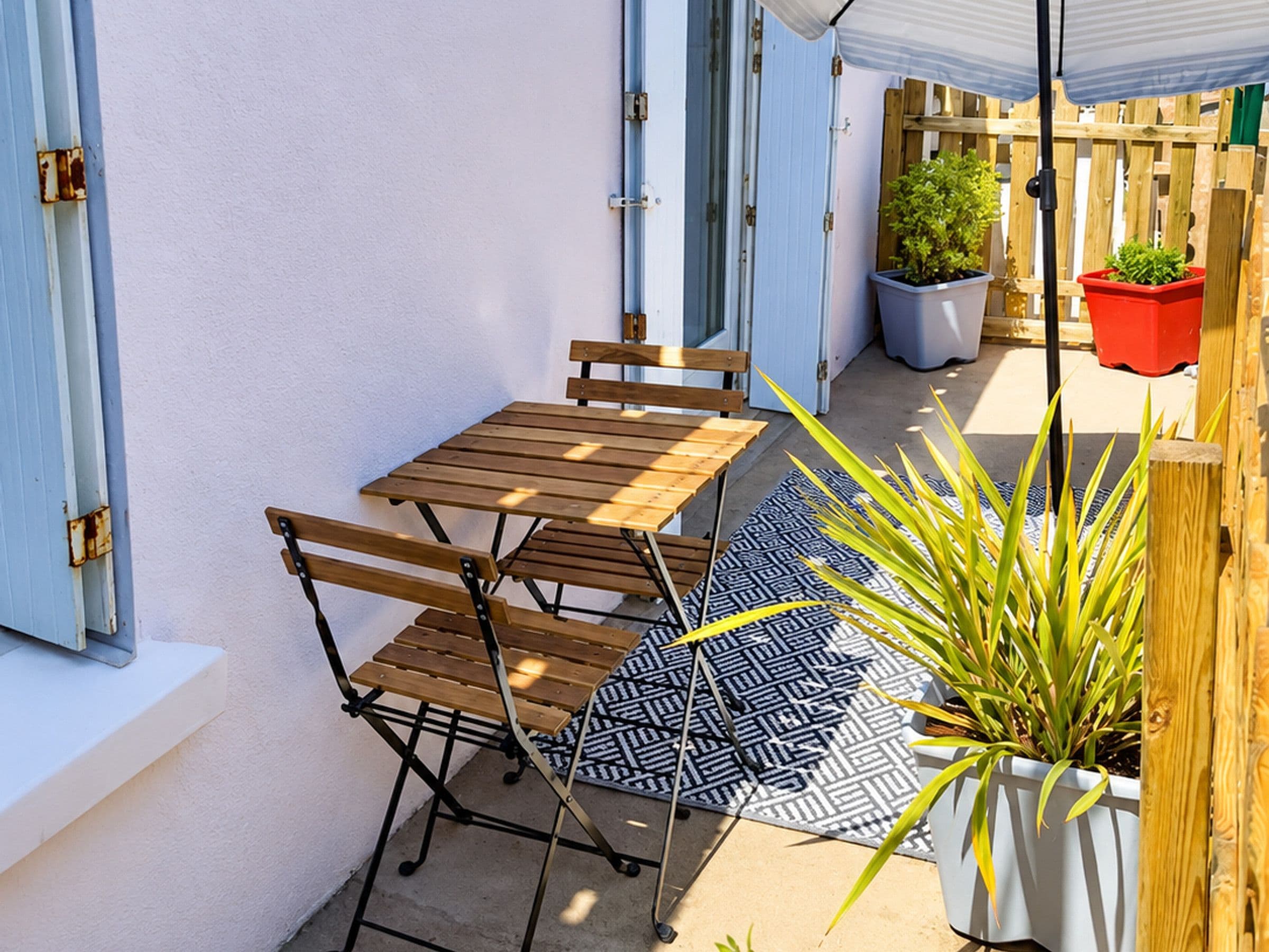 Une terrasse avec une table et des chaises en bois, un tapis à motifs et des plantes en pot.