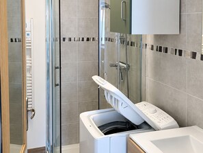 Ein modernes Badezimmer mit Duschkabine aus Glas, einer integrierten Waschmaschine und einem Schrank über dem Waschbecken.