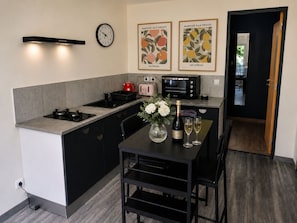 A modern kitchen with a built-in stove, a microwave, and a toaster. There is a dining table with chairs and a vase of flowers. A clock and two framed posters are on the wall. - The French Hideaway, Eymet, Pool, Parking & King or Twin Bed (eymet)