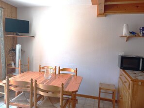 Una mesa de madera con sillas, un televisor en un estante, un microondas y un mueble pequeño.