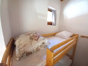 A single-occupancy room with a wooden bunk bed, a small window with curtains, and a plain white wall. - Duplex mountain view - 4 guests (Le Biot)