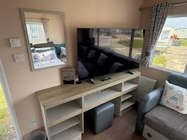 Una sala de estar moderna con un televisor de pantalla plana grande, un sofá, una mesa de centro y un ventanal con cortinas.