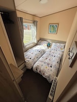 Una habitación pequeña y funcional con dos camas, una ventana con cortinas, un radiador y un cuadro colgado en la pared.