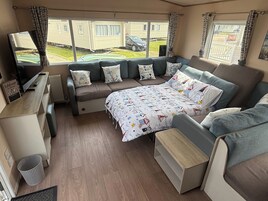 Interior acogedor de una autocaravana con cama, zona de estar y ventana con vistas a un barrio residencial.