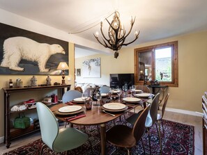 A dining room with a round table set for six, a mounted polar bear on the wall, and a chandelier. - Spacious chalet in Bozel - 10 guests (Bozel)