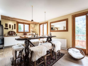 A modern kitchen with a central island, wooden stools, and a large window providing a view of the outdoors. - Spacious chalet in Bozel - 10 guests (Bozel)