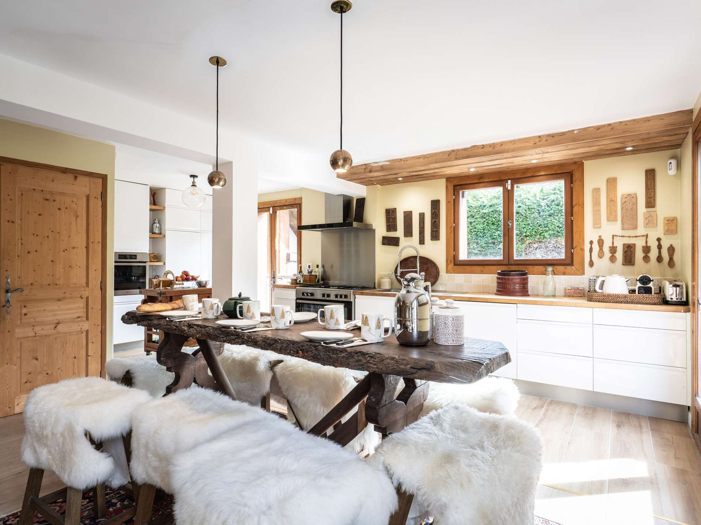 Una cucina con un tavolo di legno, sgabelli bianchi e lampade a sospensione.