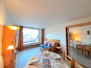 Ein Hotelzimmer mit Esstisch für zwei Personen, einem blauen Sofa, einem kleinen Nachttisch und einem großen Spiegel, der den Essbereich reflektiert.