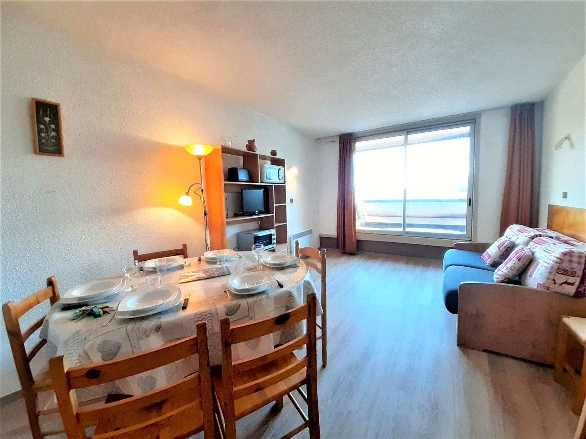 Een eetgedeelte met een tafel voor vier personen, een bank en een televisie op de achtergrond.