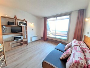 Ein Zimmer mit einem Bett, einem Fernseher, einer Mikrowelle und einem Fenster mit Vorhängen.
