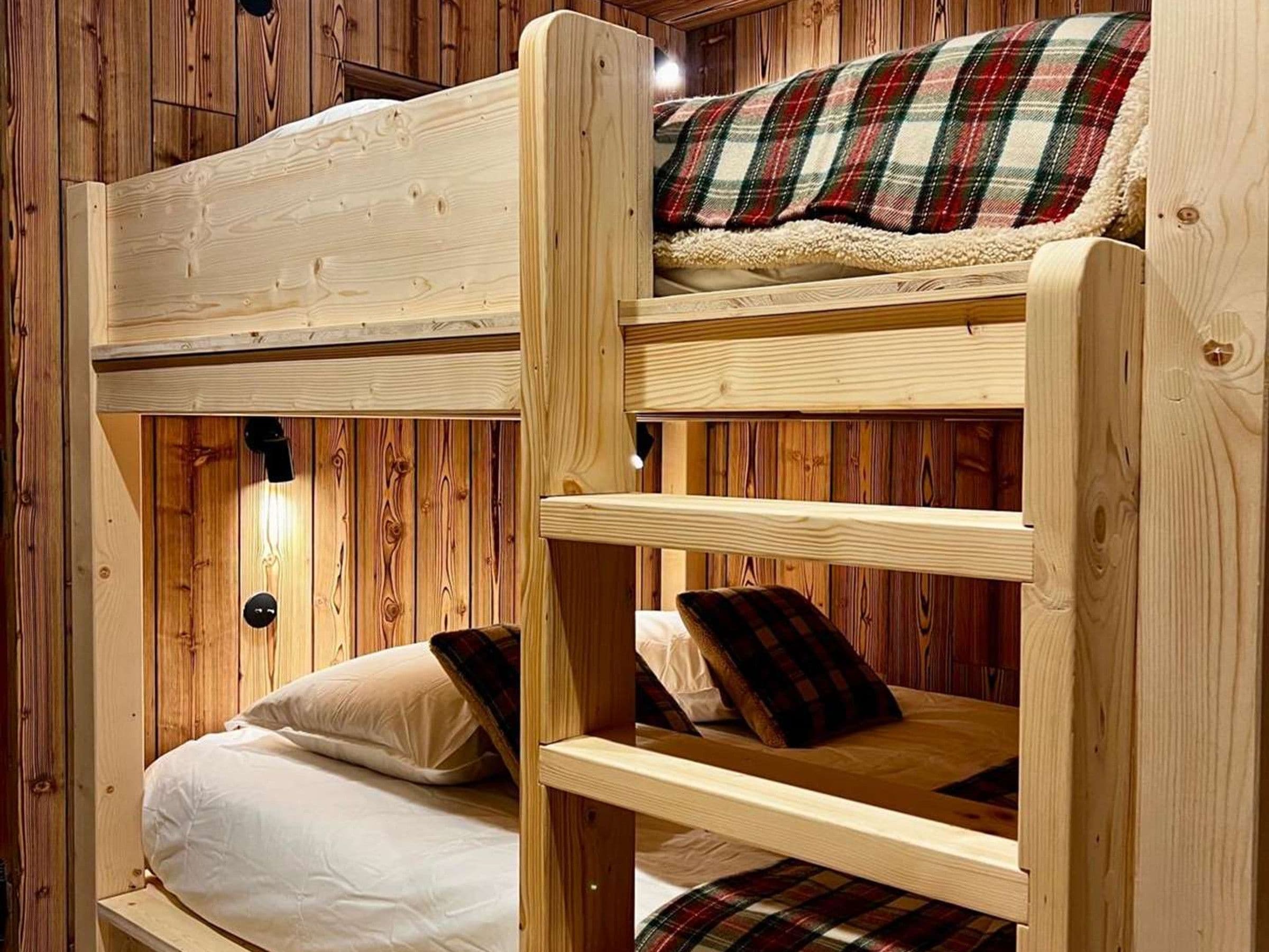 A bunk bed with a plaid blanket and pillows, wooden walls, and a light fixture.