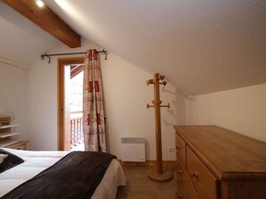 A bedroom with a bed, a wooden dresser, a coat rack, and a window with curtains. - Duplex near slopes - 8 guests (Valloire)