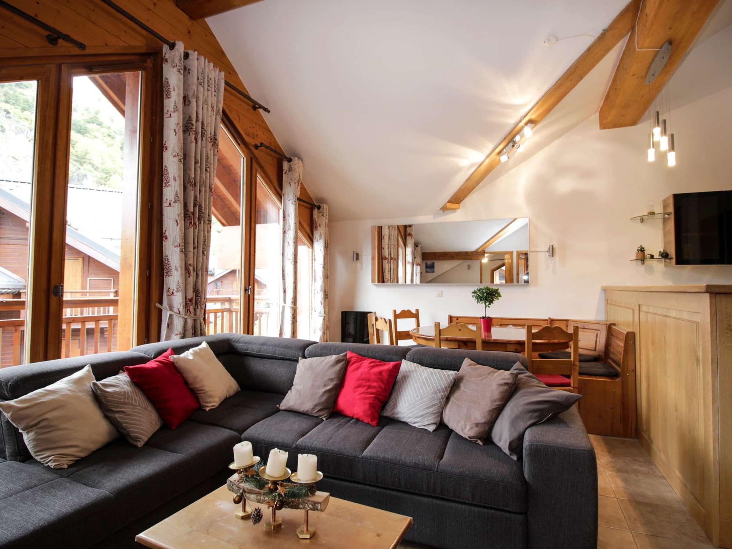 Ein gemütliches Wohnzimmer mit einem dunkelgrauen Sofa, einem Holztisch mit Kerzen und einem Essbereich mit Holzmöbeln.