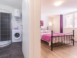 A bedroom with a bed, a window with curtains, a washing machine, and a shower area. - Denise With a Pleasant Terrace (Liznjan)