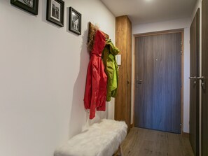 Corredor com um banco, um cabideiro com jaquetas e uma porta de madeira.