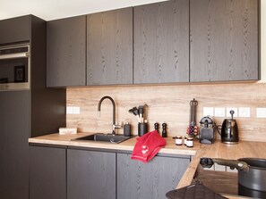A modern kitchen with dark wood cabinets, a stainless steel sink, and various appliances including a coffee maker and a kettle. - Spacious apartment, glacier view - 4 guests (Les Deux Alpes)