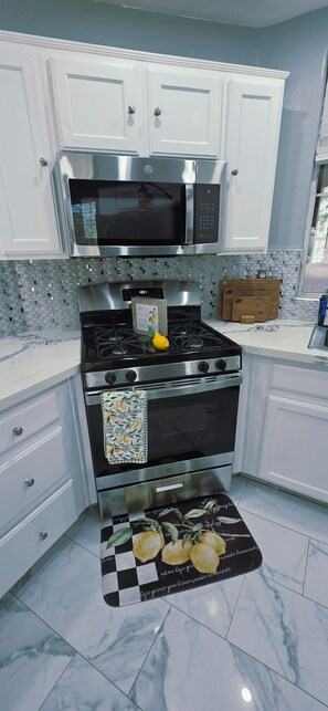 A kitchen with white cabinets, a stainless steel microwave, a gas stove, and a checkered mat with lemons. - Deluxe 4-bedroom home with AC in pleasant Las Vegas l. A perfect retreat for you (Las Vegas)