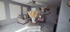 A living room with a grey sofa, a white coffee table, and a decorative vase with pampas grass. - Deluxe 4-bedroom home with AC in pleasant Las Vegas l. A perfect retreat for you (Las Vegas)