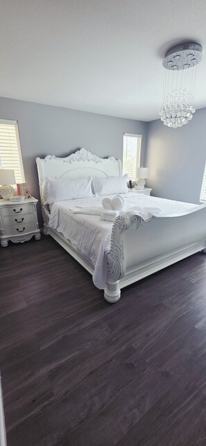 A bedroom with a large bed, a nightstand, a chandelier, and a window with blinds. - Deluxe 4-bedroom home with AC in pleasant Las Vegas l. A perfect retreat for you (Las Vegas)
